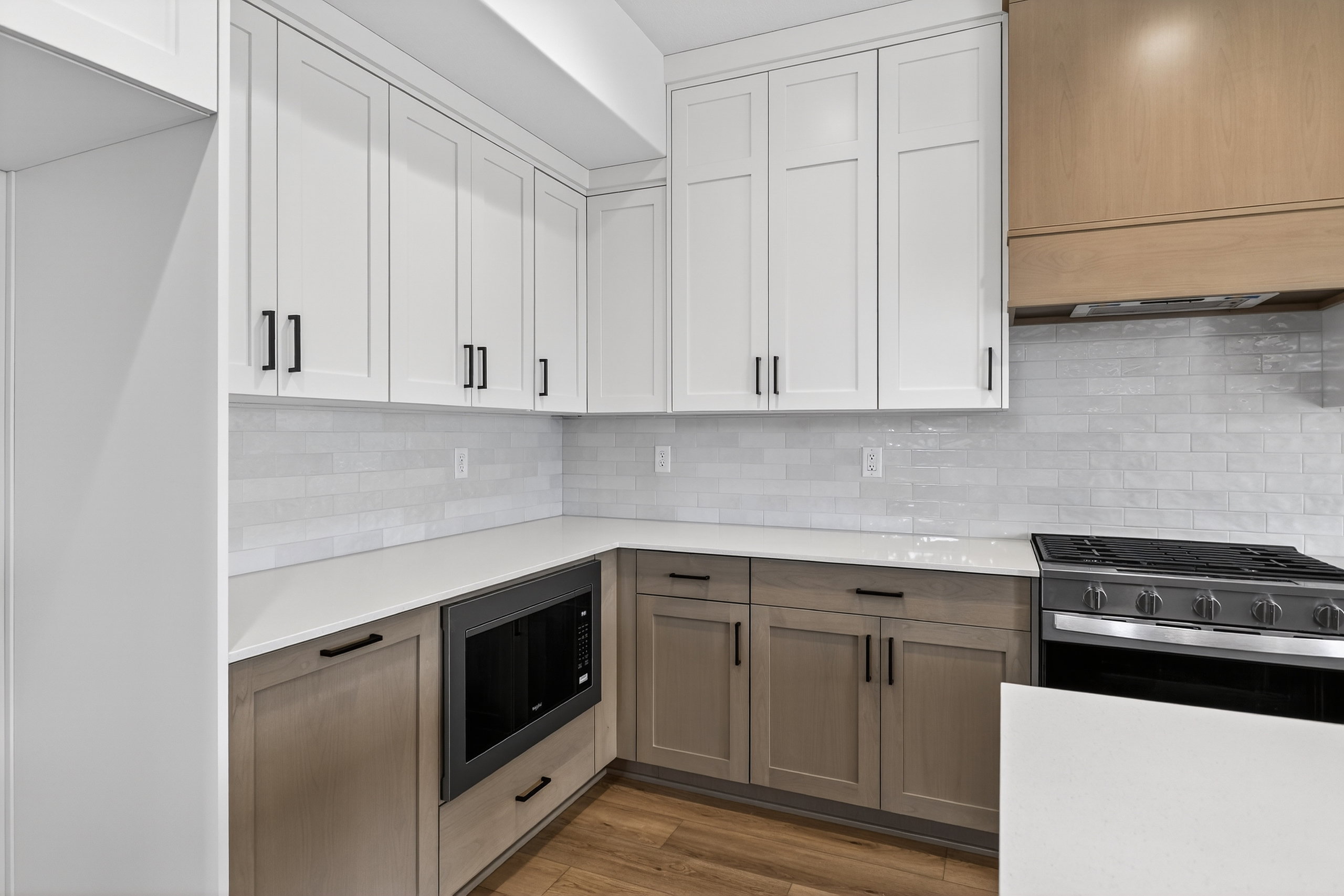 Kitchen featuring two tone color scheme, gas stove, black microwave, wood finished floors, and decorative backsplash