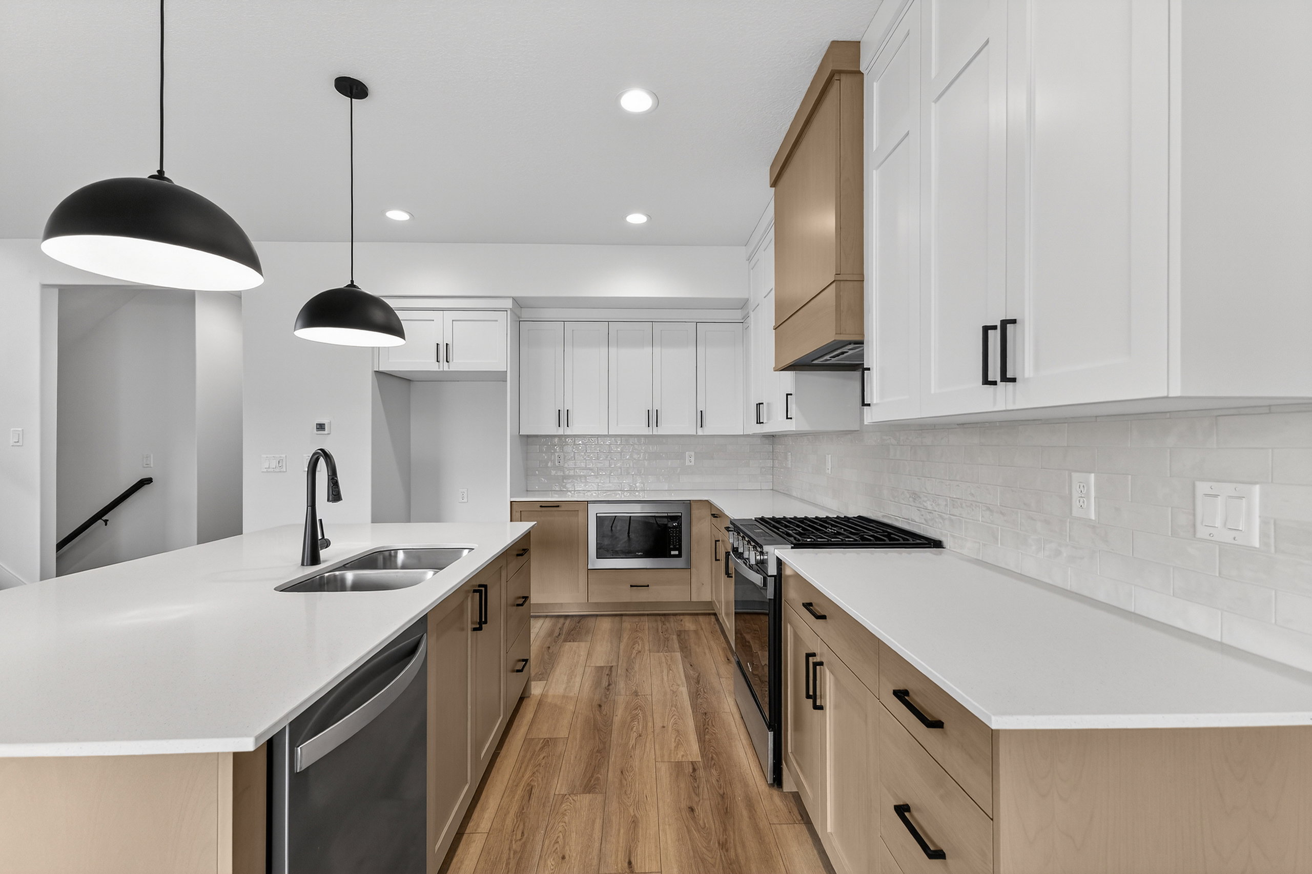 Two tone kitchen featuring a kitchen island with sink, stainless steel appliances, dual tone cabinets, light wood-type flooring, and hanging light fixtures