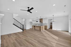 Unfurnished living room with ceiling fan, a chandelier, and light wood-style floors