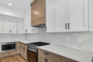 Kitchen featuring stainless steel gas range oven, dual tone cabinets, built in microwave, tasteful backsplash, and light stone countertops