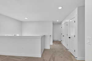 Hall with light colored carpet, recessed lighting, and an upstairs landing