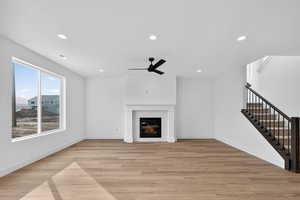Unfurnished living room featuring light wood-style floors, a ceiling fan, recessed lighting, and a tile fireplace