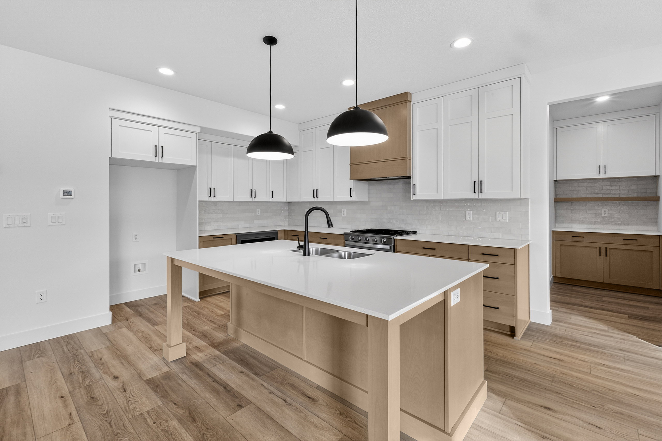 Two tone kitchen with an island with sink, dual tone cabinetry, light wood-style floors, hanging light fixtures, and tasteful backsplash