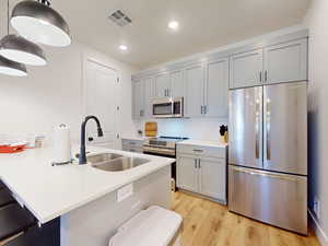 Kitchen featuring stainless steel appliances, gray cabinetry, a kitchen breakfast bar, light wood finished floors, and light stone counters