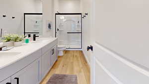 Bathroom featuring a shower stall, double vanity, and light wood finished floors