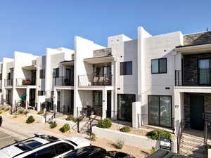 Rear view of house featuring stone siding, stucco siding, a balcony, and a residential view