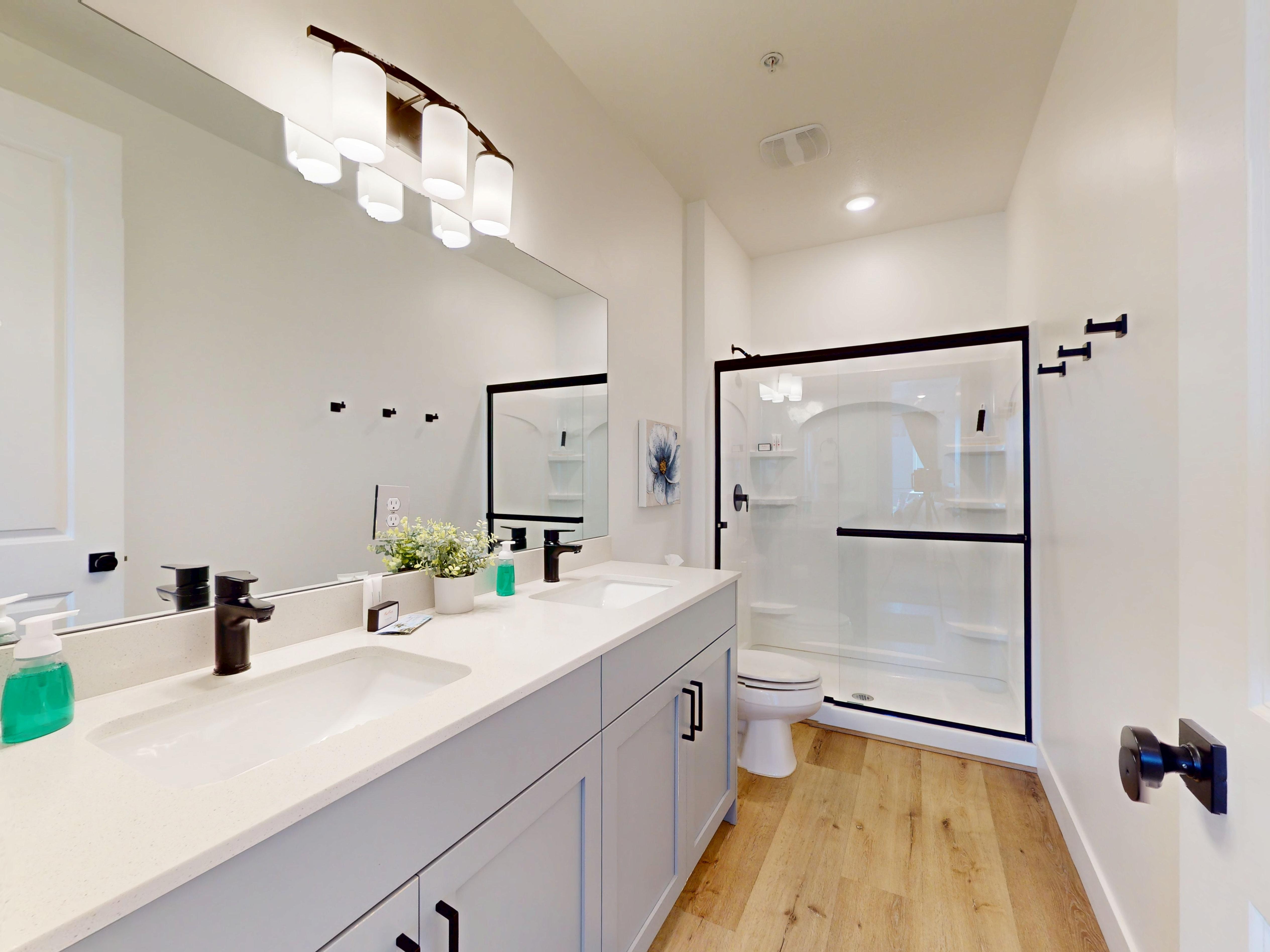 Bathroom featuring a shower stall, double vanity, and light wood finished floors