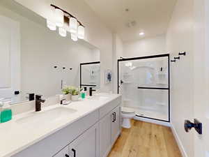 Bathroom featuring a shower stall, double vanity, and light wood finished floors