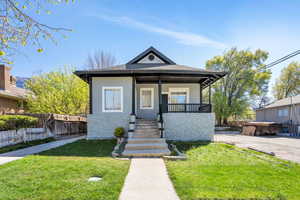 View of front facade featuring a porch, stucco siding, a front yard, and stone siding