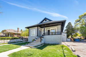 View of front facade featuring a porch, a front lawn, stucco siding, and stone siding