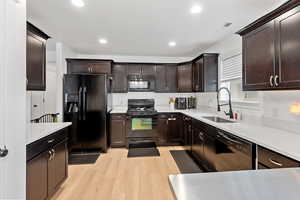 Kitchen featuring dark wood finish cabinetry, black appliances, light wood-type flooring, recessed lighting, and light stone countertops