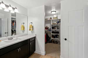 Bathroom featuring a walk in closet, vanity, a textured ceiling, and light wood finished floors