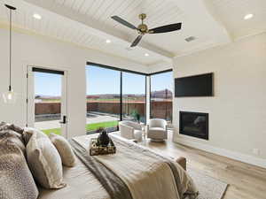 Bedroom with access to outside, light wood finished floors, beam ceiling, a glass covered fireplace, and ceiling fan