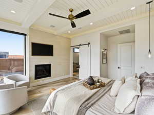 Bedroom with a barn door, wood finished floors, a fireplace, ceiling fan, and recessed lighting