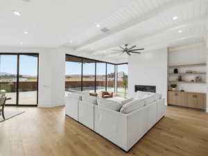 Living room with beamed ceiling, light wood-style flooring, a glass covered fireplace, a ceiling fan, and plenty of natural light