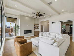 Living area featuring a barn door, a ceiling fan, beamed ceiling, hardwood / wood-style floors, and recessed lighting