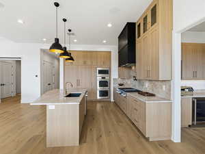 Kitchen featuring light wood finish cabinets, light stone counters, a large island, light wood-style flooring, and decorative light fixtures