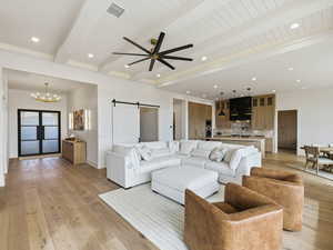 Living area with a barn door, beamed ceiling, a ceiling fan, light wood-style floors, and hanging lights