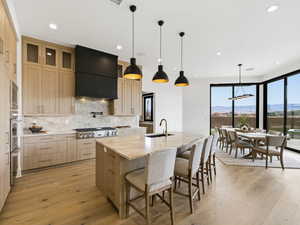 Kitchen featuring light wood finish cabinets, light stone countertops, a kitchen bar, hanging light fixtures, and light wood-style flooring