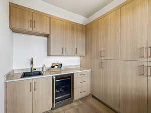 Bar area with wine cooler, wood finished floors, light wood finish cabinetry, light stone countertops, and modern cabinets