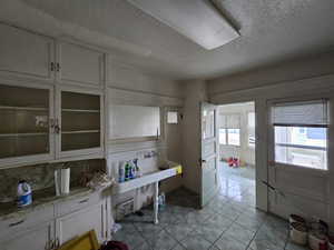 Kitchen featuring white cabinetry, a textured ceiling, glass fronted cabinets, backsplash, and light tile patterned floors