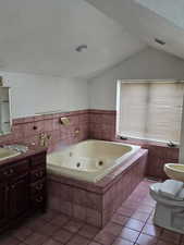 Full bath featuring vanity, a jetted tub, and dark tile patterned flooring