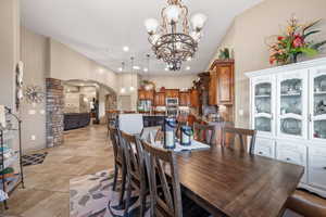 Dining space with arched walkways, hanging lights, decorative columns, light tile patterned floors, and a high ceiling