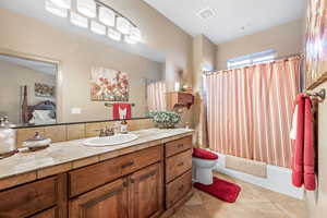 Ensuite bathroom featuring vanity, shower / tub combo with curtain, and light tile patterned floors
