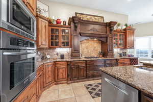 Kitchen featuring glass fronted cabinets, stainless steel appliances, dark stone countertops, and light tile patterned floors