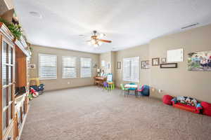 Playroom with ceiling fan, carpet, and a textured ceiling