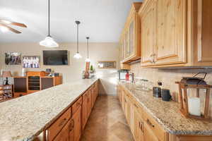 Kitchen with light stone countertops, hanging light fixtures, a peninsula, glass fronted cabinets, and decorative backsplash