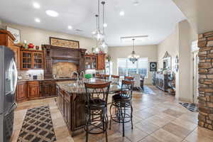 Kitchen with glass fronted cabinets, dark stone counters, stainless steel fridge with ice dispenser, a breakfast bar, and a center island with sink