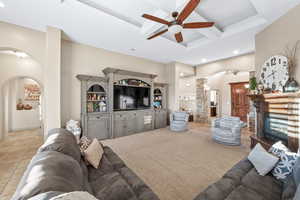 Living area featuring arched walkways, coffered ceiling, ceiling fan, recessed lighting, and a fireplace