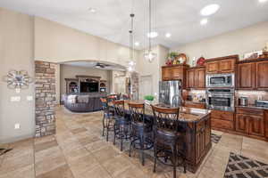 Kitchen with a kitchen breakfast bar, dark stone countertops, decorative light fixtures, a ceiling fan, and a kitchen island with sink