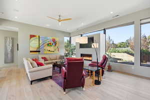 Living room with ceiling fan, a glass covered fireplace, light wood-type flooring, and recessed lighting