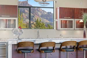 Kitchen featuring modern cabinets, a mountain view, light stone countertops, a breakfast bar, and glass fronted cabinets