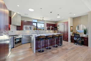 Kitchen featuring a breakfast bar, double oven range, light wood-style floors, an office area, and paneled built in fridge