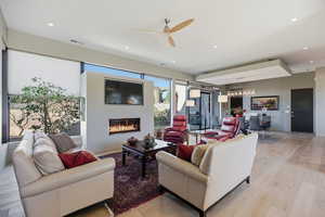 Living room with light wood-style floors, a ceiling fan, a glass covered fireplace, and a chandelier