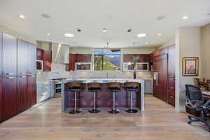 Kitchen featuring a breakfast bar, reddish brown cabinets, stainless steel appliances, light wood finished floors, and a kitchen island