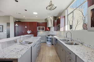 Kitchen featuring light stone counters, modern cabinets, stainless steel appliances, light wood-style floors, and hanging light fixtures