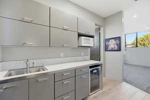 Kitchen featuring gray cabinetry, light countertops, beverage cooler, white microwave, and light wood-style flooring