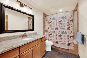 Bathroom featuring vanity, shower / tub combo with curtain, dark stone finish flooring, and recessed lighting