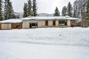 View of front facade with stucco siding, stone siding, a standing seam roof, and a wooden deck