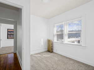 Carpeted empty room with radiator heating unit and baseboards