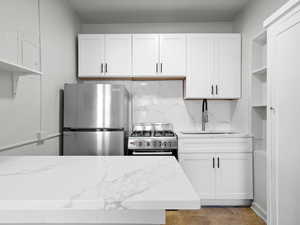 Kitchen featuring open shelves, light stone countertops, stainless steel appliances, and white cabinetry