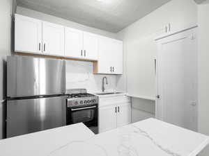 Kitchen featuring freestanding refrigerator, backsplash, range with gas cooktop, white cabinets, and light stone countertops