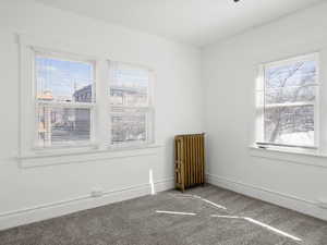 Empty room featuring radiator heating unit, carpet, and healthy amount of natural light
