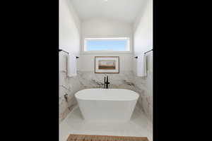 Bathroom with a soaking tub, lofted ceiling, tile walls, and a wainscoted wall