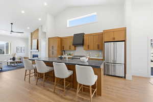 Kitchen with high end refrigerator, wood finish cabinetry, a stone fireplace, light wood-style flooring, and lofted ceiling