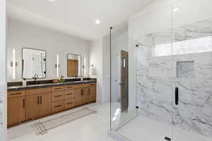 Full bath with double vanity, a marble finish shower, and recessed lighting